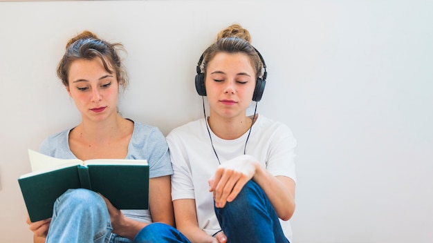 Foto gratuita libro de lectura de mujer sentada cerca de la mujer escuchando música en auriculares