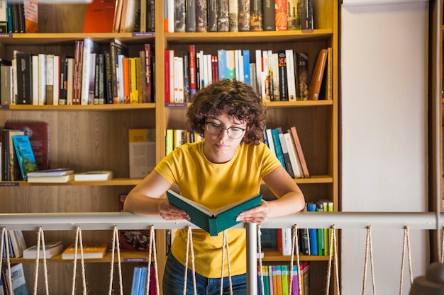 Libro de lectura pensativo joven de la mujer en biblioteca