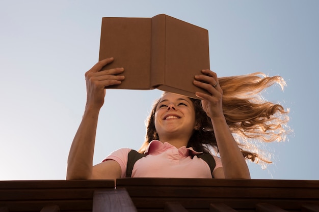 Libro de lectura rubio joven sonriente en luz del sol