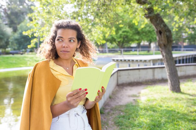 Libro de lectura serio de la mujer joven en parque de la ciudad