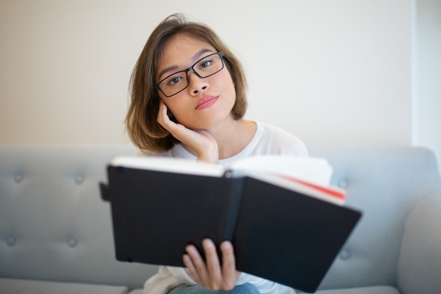 Libro de lectura serio de la señora joven en el sofá en casa