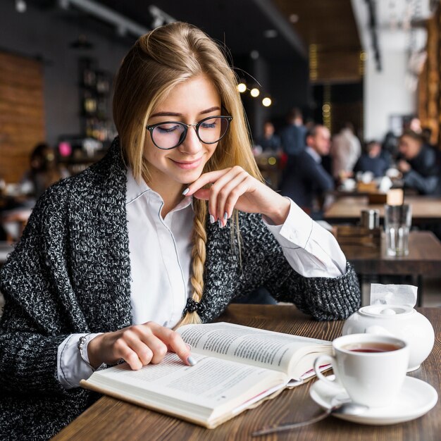 Libro de lectura sonriente de la mujer en café