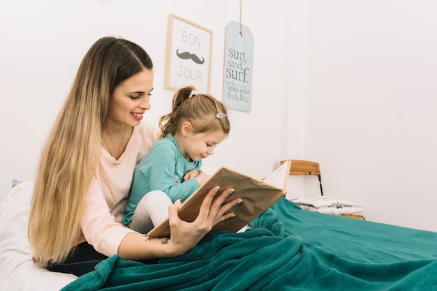 Libro de lectura sonriente de la mujer a la hija en la cama