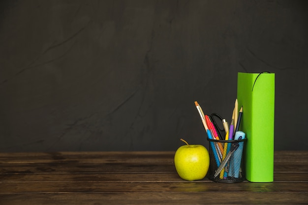 Libro con taza de lápiz y manzana en el escritorio