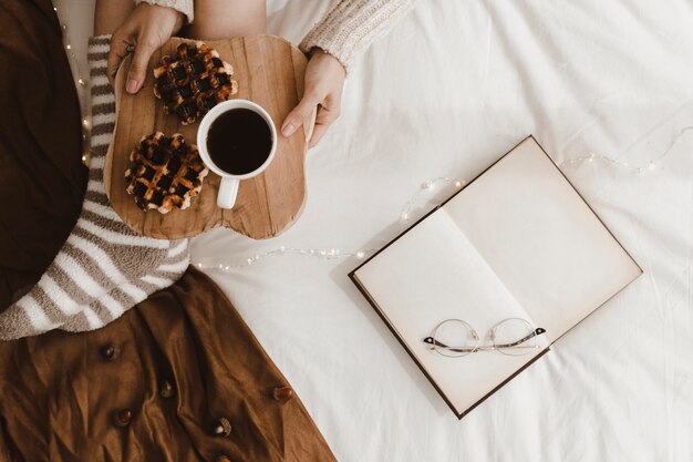 Libro y vasos cerca de mujer con postre y bebida