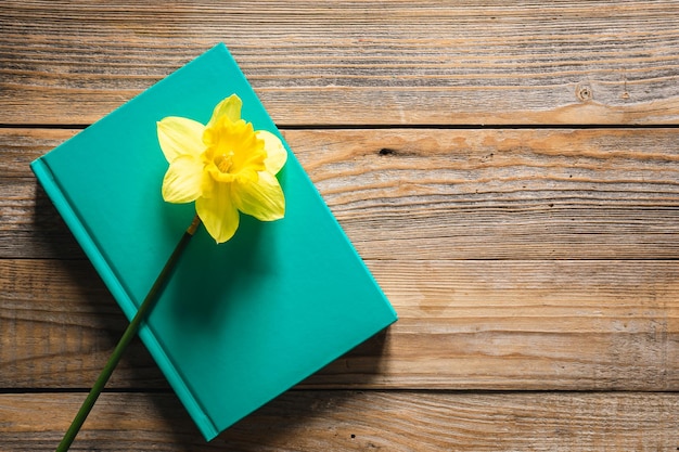 Foto gratuita libro verde y flor de narciso amarillo en la vista superior de fondo de madera