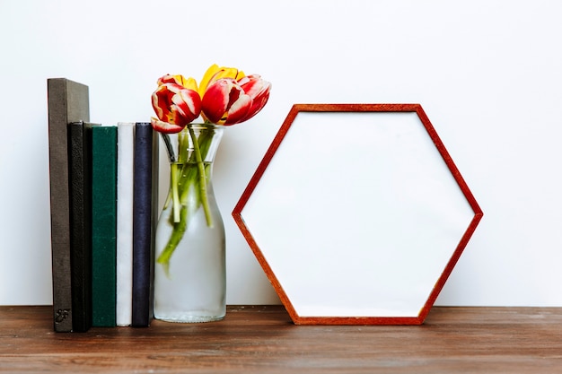 Libros y florero cerca del marco hexagonal