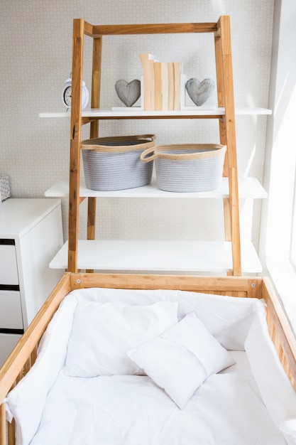 Libros, forma de corazón y dispuestos en la cesta estante cerca de la cuna en la habitación de la cama