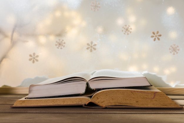 Libros en mesa de madera cerca de banco de nieve, copos de nieve y luces de colores