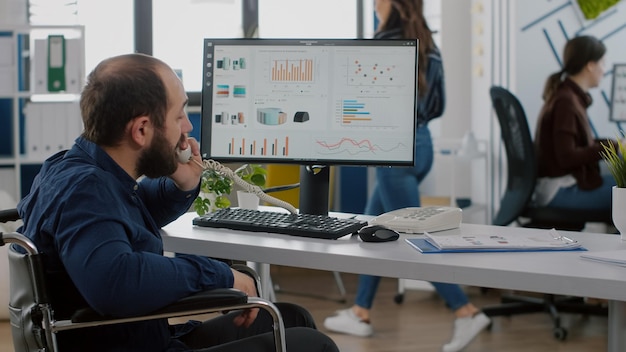 Foto gratuita líder del equipo discapacitado paralizado ocupado contestando el teléfono hablando con el socio escribiendo en la computadora explicando la idea del proyecto y verificando los datos financieros. diversos colegas que trabajan en la oficina de puesta en marcha