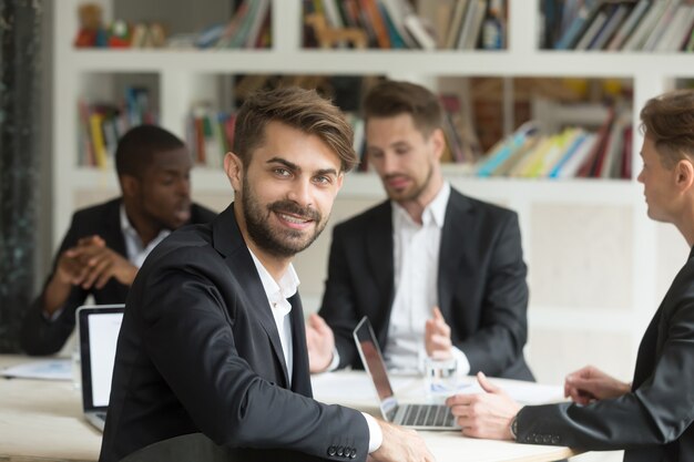 Líder de equipo sonriente que mira la cámara en la reunión corporativa del grupo