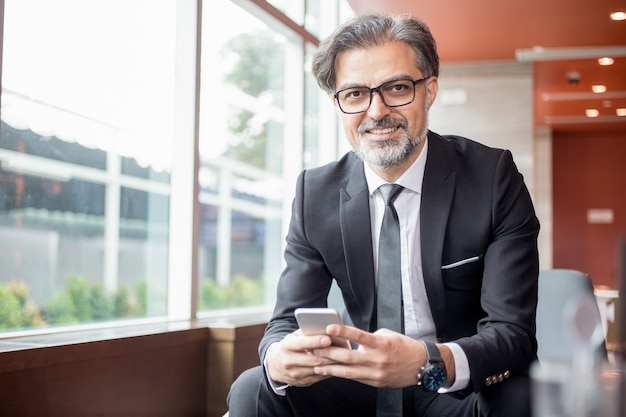 Líder de negocios feliz usando el teléfono inteligente en el vestíbulo