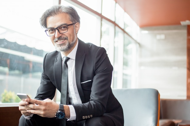 Líder de negocios sonriente utilizando el teléfono inteligente en el vestíbulo