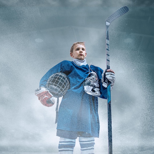 Líder. Pequeño jugador de hockey con el palo en la cancha de hielo y fondo de humo. Deportista con equipo y entrenamiento con casco en acción. Concepto de deporte, infancia, movimiento, movimiento, acción.