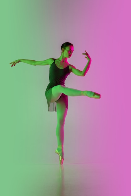 Ligero. Bailarina de ballet joven y elegante aislada en la pared rosa-verde degradada en neón. Arte, movimiento, acción, flexibilidad, concepto de inspiración. Bailarina flexible, saltos ingrávidos.