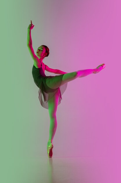 Ligero. Bailarina de ballet joven y elegante aislada en la pared rosa-verde degradada en neón. Arte, movimiento, acción, flexibilidad, concepto de inspiración. Bailarina flexible, saltos ingrávidos.