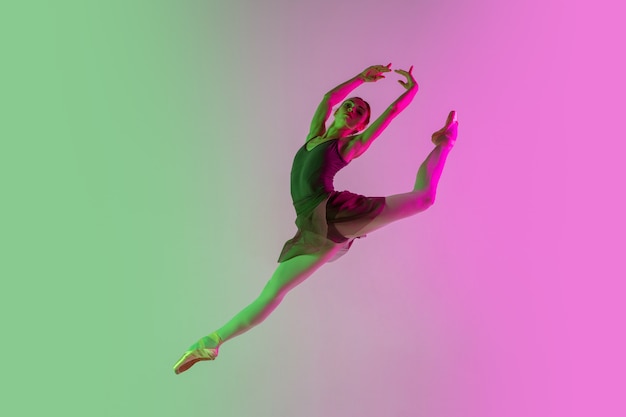 Ligero. Bailarina de ballet joven y elegante aislada en la pared rosa-verde degradada en neón. Arte, movimiento, acción, flexibilidad, concepto de inspiración. Bailarina flexible, saltos ingrávidos.