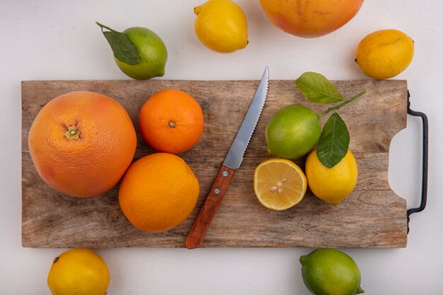 Lima vista superior con limones naranjas y pomelo en una tabla con un cuchillo sobre un fondo blanco.