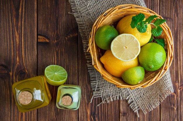 Limas con limones, refrescos, hierbas en una cesta de mimbre en madera y saco, aplanada.