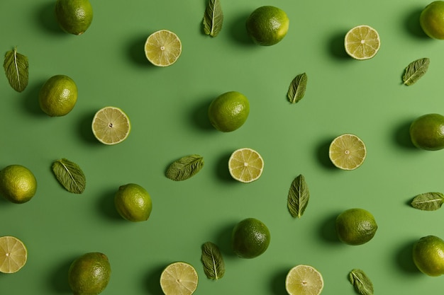 Limas verdes ácidas brillantes cargadas de nutrientes y menta fresca sobre fondo verde. Los cítricos pueden estimular su sistema inmunológico y promover una piel sana. Aroma floral de ralladura, ingredientes apreciados para el jugo.