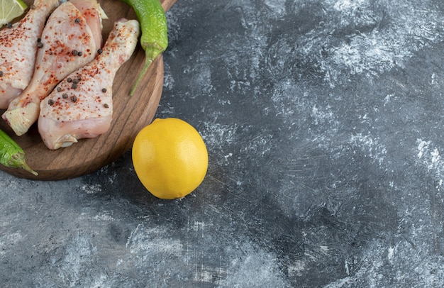 Limón amarillo fresco y muslos de pollo crudo sobre tabla de madera.