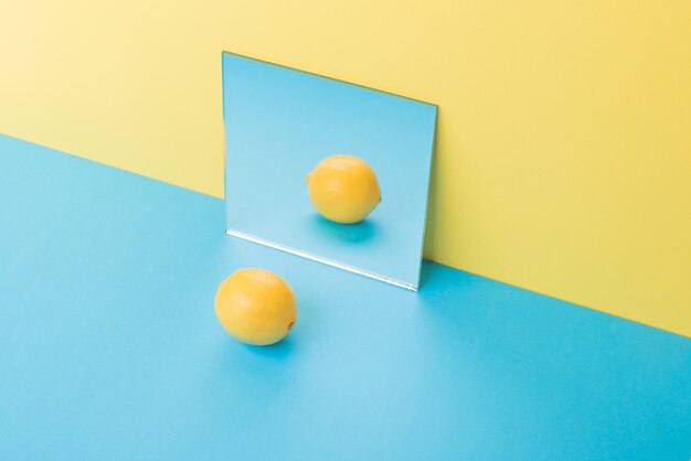 Limón en mesa azul aislado en amarillo cerca del espejo
