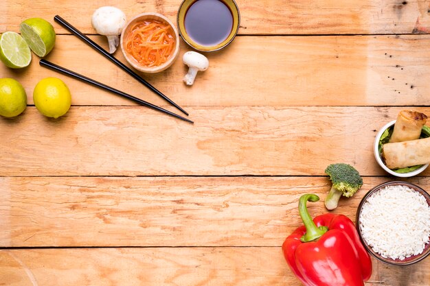 Limón; palillos; seta; salsas Pimientos; brócoli; Arroz y rollitos de primavera sobre tabla de madera.