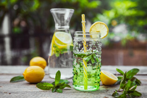 Limonada e ingredientes en jarra de vidrio y tarro en mesa de madera y jardín. vista lateral.