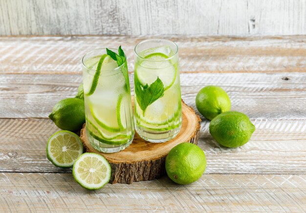 Limonada helada con limones, albahaca, madera en vasos en madera y sucio, vista de ángulo alto.