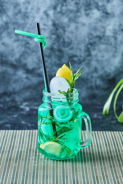 Limonada con limón, hielo, paja y menta en la superficie oscura