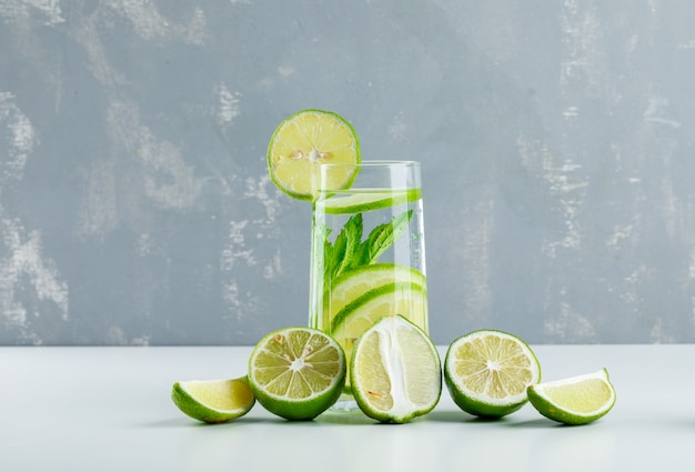 Limonada con limones, hierbas en un vaso sobre yeso y blanco