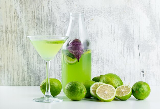 Limonada con limones, hojas de albahaca en vidrio y botella en blanco y sucio,