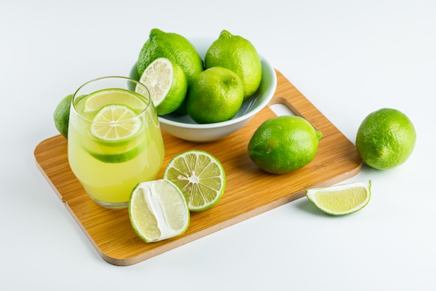 Limonada con limones en un vaso en blanco y tabla de cortar, vista de ángulo alto.