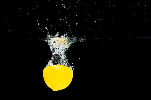 Foto gratuita limonada a la mitad cayendo en agua limpia sobre fondo negro