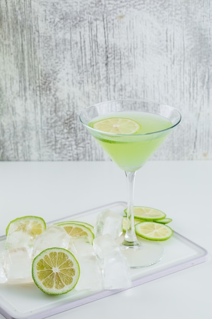 Foto gratuita limonada en un vaso con limón, tabla de cortar, cubitos de hielo vista lateral en blanco y sucio