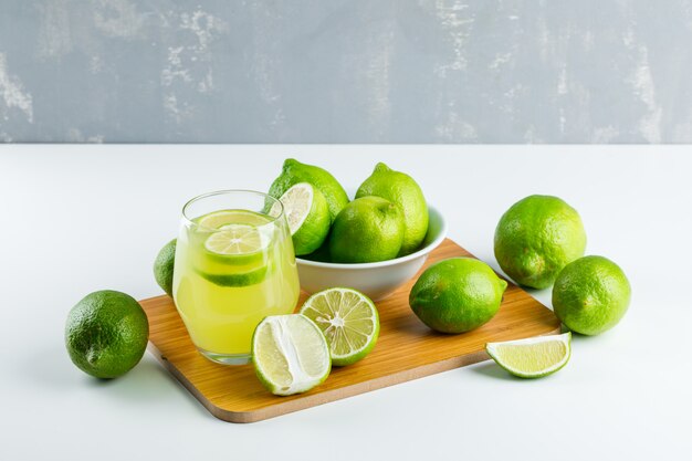 Limonada en un vaso con limones, tabla de cortar vista de ángulo alto en blanco y yeso