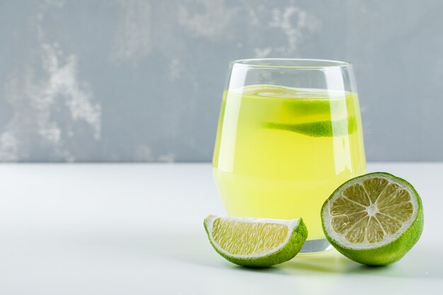 Limonada en un vaso con vista lateral de limón en blanco y yeso