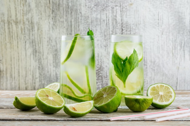 Limonada en vasos con limón, albahaca, pajas vista lateral en madera y sucio