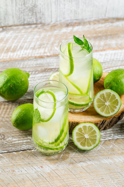 Limonada en vasos con limón, albahaca, tabla de cortar vista de ángulo alto en madera y sucio