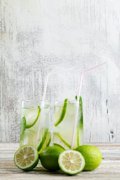 Limonada en vasos con limón, vista lateral de albahaca en madera y sucio