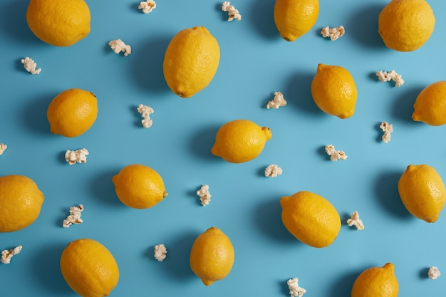 Limones amarillos maduros agrios y palomitas de maíz dulces alrededor. Hermosa composición de cítricos sobre fondo azul. Fruta tropical deliciosa y saludable que contiene muchas vitaminas. Concepto de nutrición. De cerca