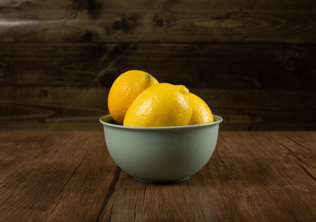 Limones amarillos en un recipiente en la mesa de madera