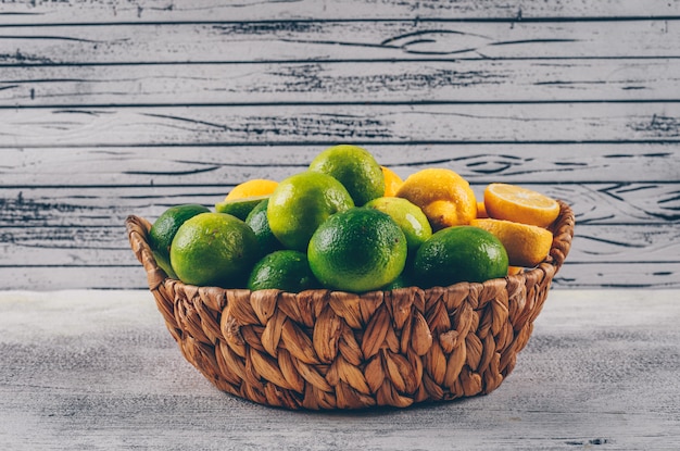 Foto gratuita limones amarillos y verdes en una cesta vista lateral sobre un fondo de madera gris