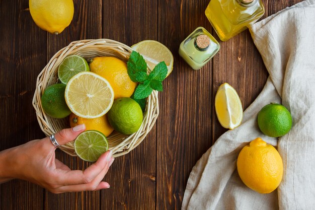 Limones en una canasta con mano de tela blanca sosteniendo la mitad de la vista superior de limón sobre una superficie de madera