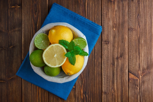 Foto gratuita limones en una canasta con vista superior de tela azul sobre una superficie de madera