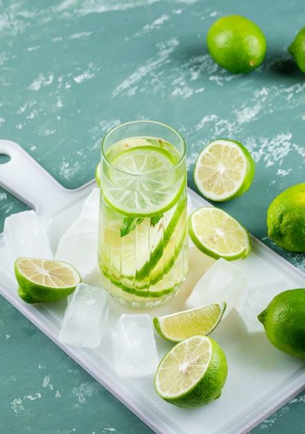 Limones con cubitos de hielo, limonada vista de ángulo alto en yeso y tabla de cortar