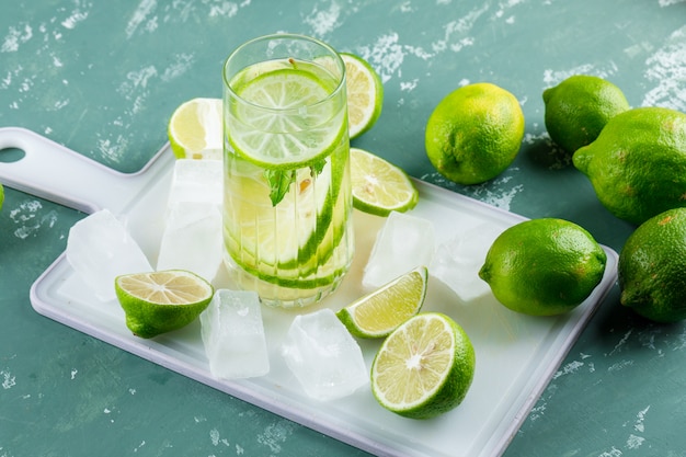 Limones con cubitos de hielo, limonada vista de ángulo alto en yeso y tabla de cortar