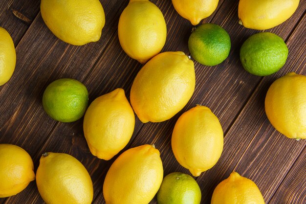 Limones dispersos con limas en una mesa de madera. aplanada