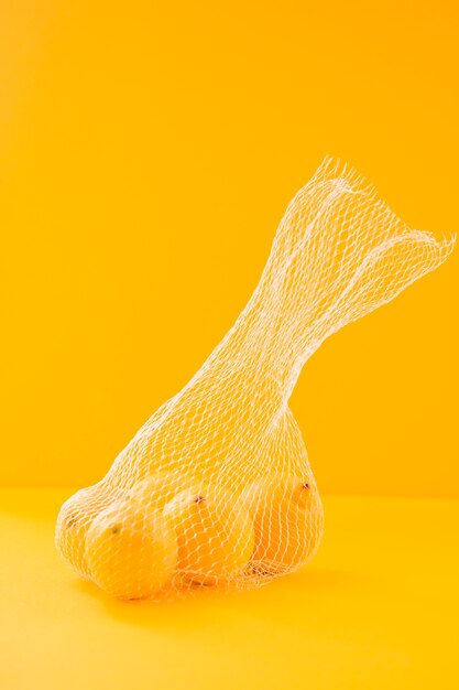 Limones enteros jugosos dentro de la red contra fondo amarillo