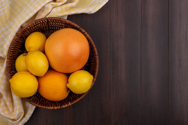Limones de espacio de copia de vista superior con naranja y pomelo en canasta con toalla a cuadros amarilla sobre fondo de madera